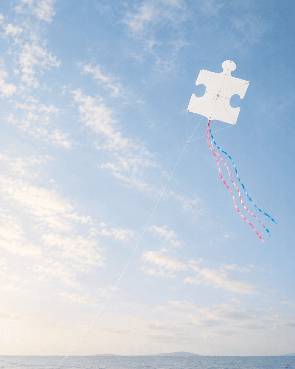 Pièce de puzzle blanche en forme de cerf-volant dans un ciel bleu lumineux, reliée par un fil et accompagnée de rubans roses et bleus, symbole de transidentité, d’identité de genre, de questionnement et d’acceptation de soi.